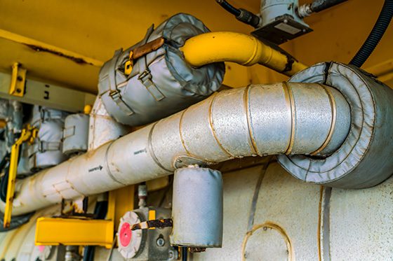 Close-up of industrial pipes with thermal insulation using traditional fastening methods, highlighting limitations in high-temperature environments.