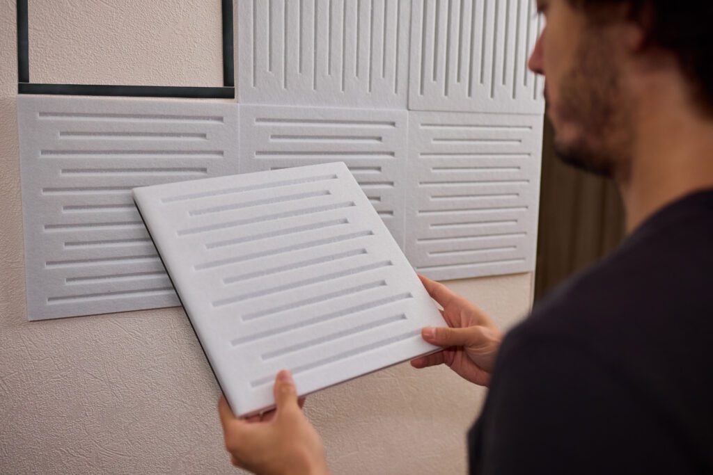 Person installing acoustic wall paneling by pressing slatted panels onto a prepared interior wall.