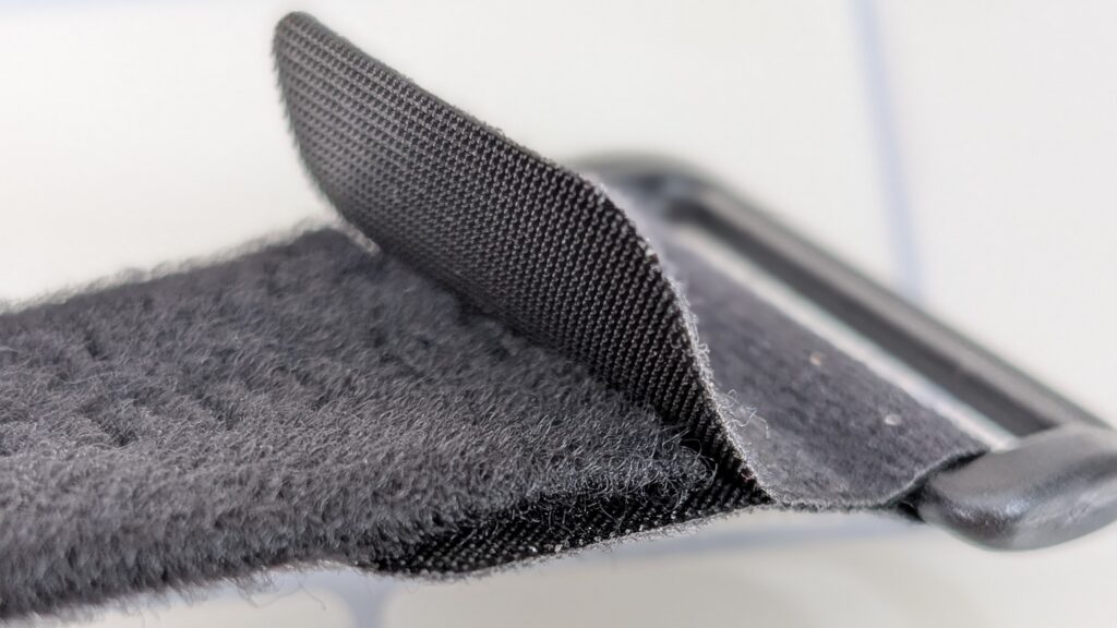 Close-up of a black VELCRO® Brand Alligator Strap being attached, with hook and loop fasteners partially engaged and threaded through a rectangular plastic buckle.