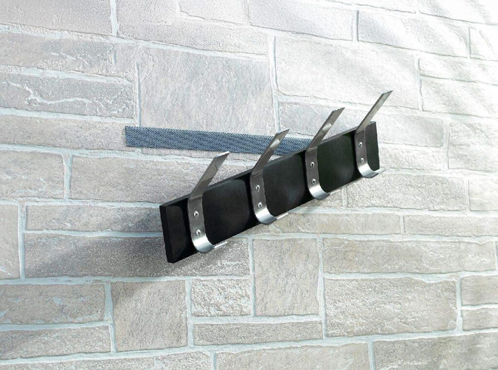 Wall-mounted coat rack with four metal hooks attached to a brick-patterned wall using VELCRO® Brand fasteners, offering a damage-free alternative to drilling.