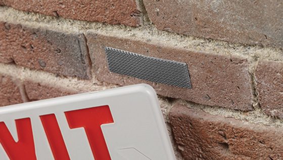 Close-up of a red and white EXIT sign being mounted on a brick wall using VELCRO® Brand fasteners, offering a secure, no-drill solution.