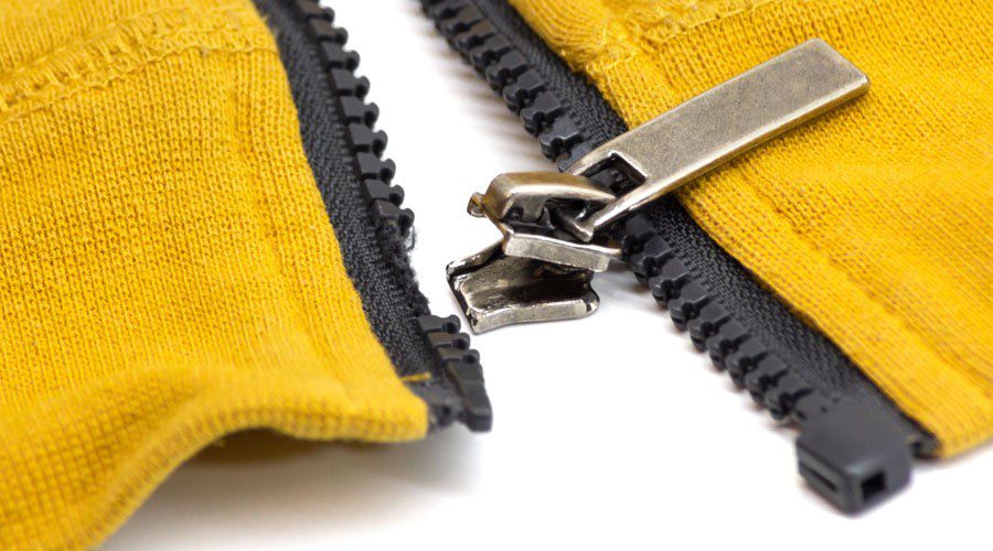 Close-up of a yellow zipper with black teeth and metallic pull, representing traditional industrial fasteners and hardware alternatives to hook and loop fasteners.