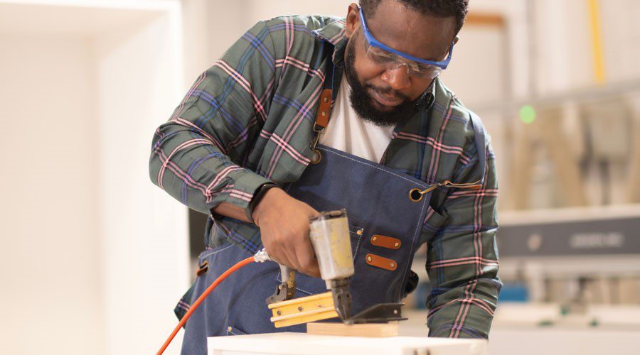 Worker using a nail gun on wood in a workshop, illustrating the risks and rigidity of traditional hardware compared to hook and loop.