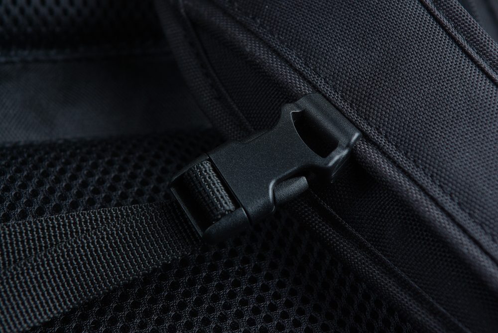 Close-up of a black plastic buckle on a backpack strap, highlighting the rigidity of traditional fasteners compared to flexible hook and loop alternatives used in a wide range of manufacturing processes.