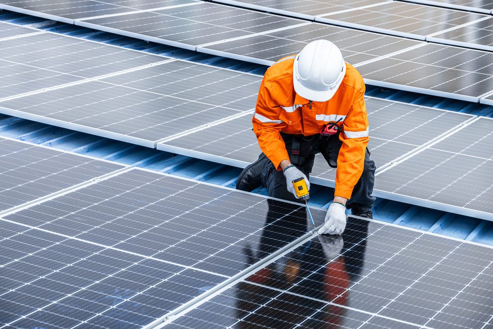 Construction worker mounting solar panels on a commercial roof using a drill