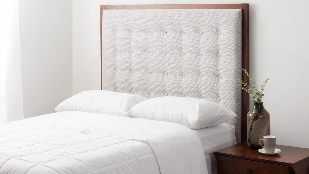 Cushioned headboard on bed with white bedding and dark wood,