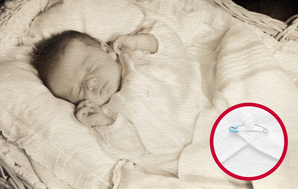 Sepia-toned photo of a sleeping baby with an inset close-up of a safety pin fastened to white fabric—highlighting how safety pins were once used to secure cloth diapers.