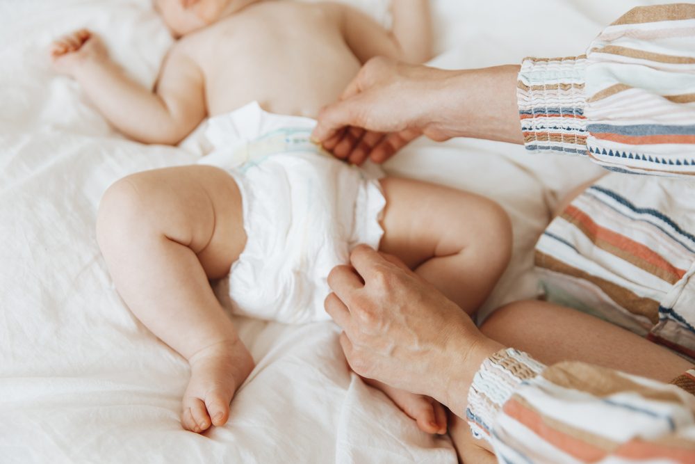 Mom fastening disposable diaper on a bed.
