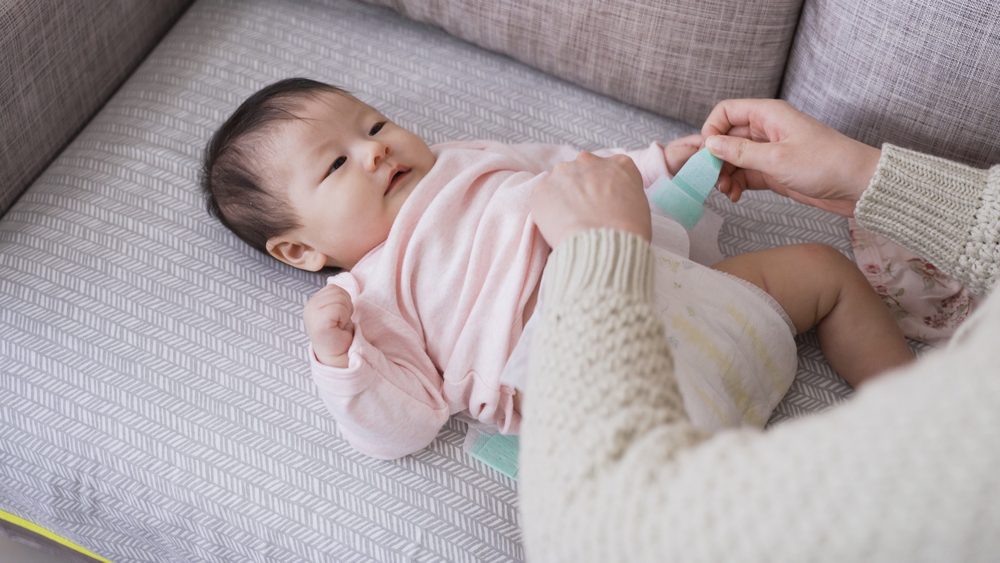Mom fastening diaper tabs while changing her baby on a sofa.