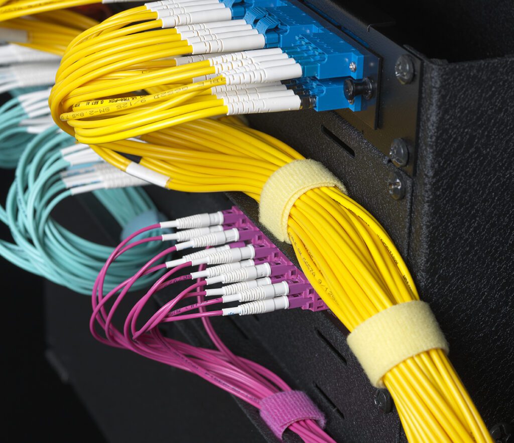 Fiber‑optic jumpers routed to patch panel ports and bundled with VELCRO® Brand ONE‑WRAP® straps.