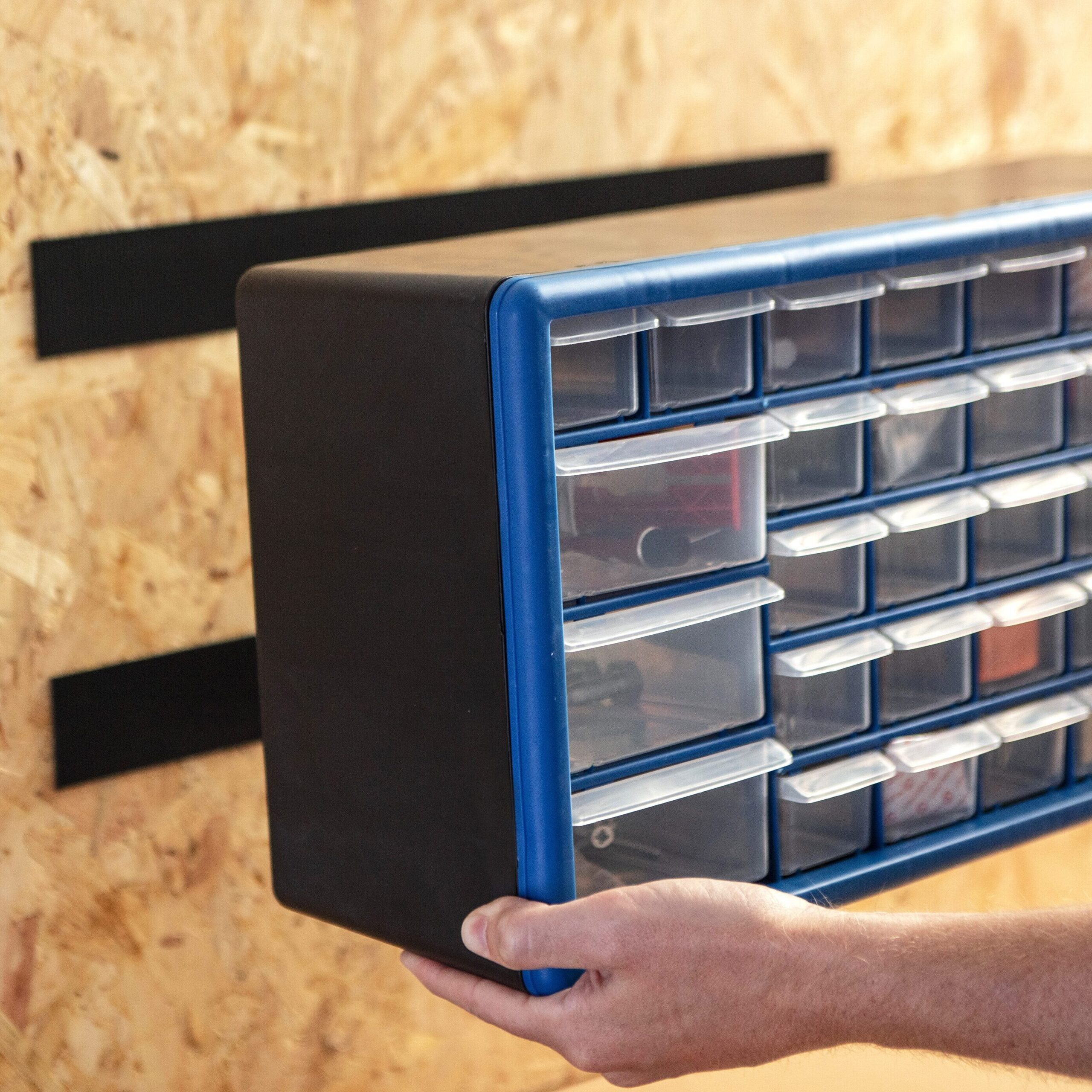 Person mounting a plastic drawer organizer onto a van wall using hook and loop fasteners for secure tool storage.
