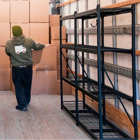 Man stacking boxes in large van with metal shelving unit.
